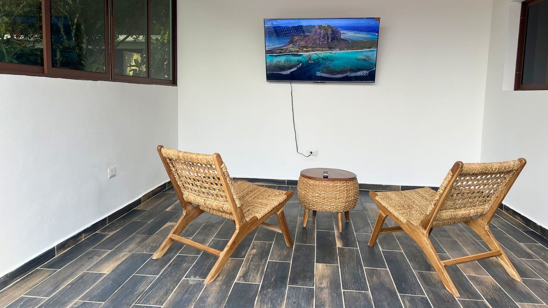 Une pièce comprenant deux fauteuils en osier, une petite table ronde et un téléviseur fixé au mur, qui diffuse une vue panoramique.