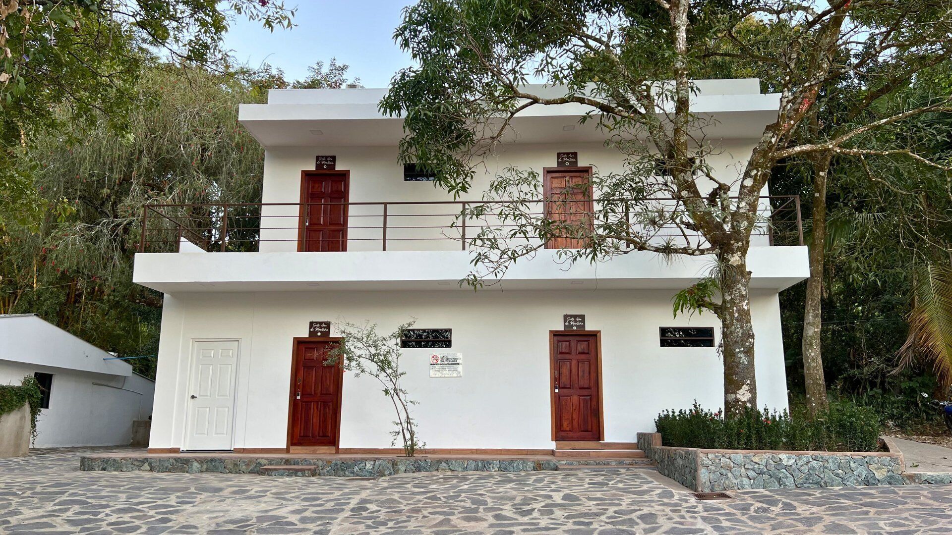 A two-story building with a white facade, two wooden doors, and a balcony.