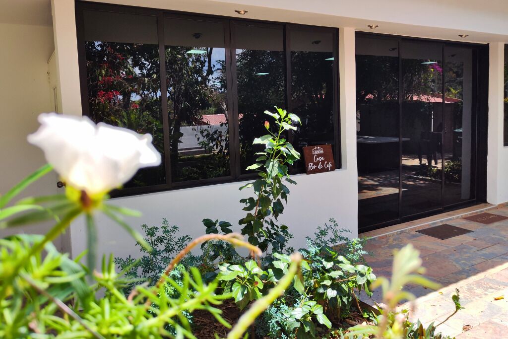 A building entrance with a sign reading "Casa Flor de Café," a patio area with plants, and a white flower in the foreground.