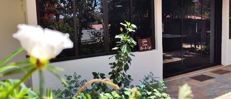 A building entrance with a sign reading "Casa Flor de Café," a patio area with plants, and a white flower in the foreground.
