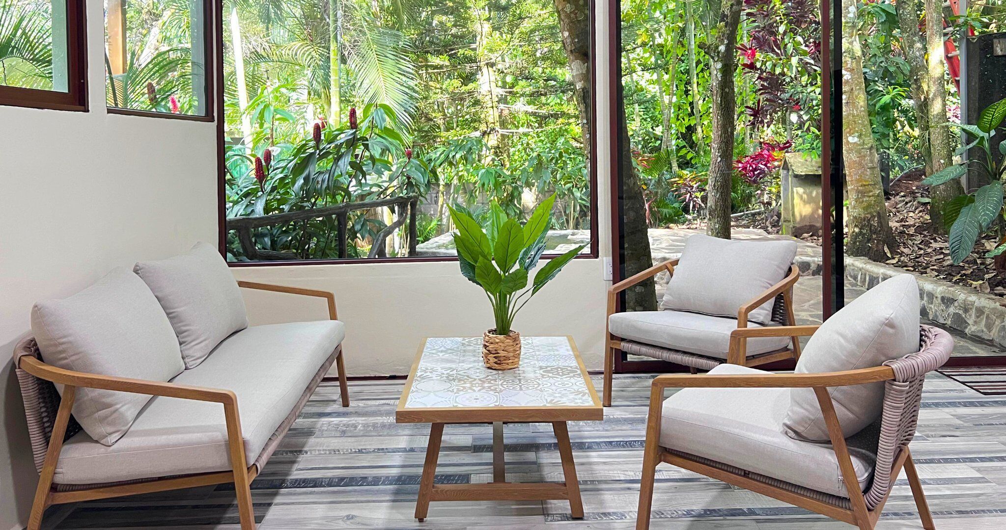 Ein Zimmer mit zwei Sofas, einem Tisch, einer Topfpflanze und Blick auf üppiges Grün durch große Fenster.