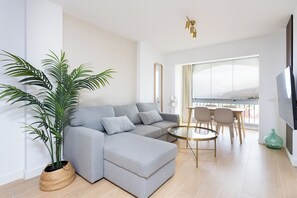 A modern living room with a grey sectional sofa, a round coffee table, and a large potted plant. - Home2Book Serenity Terrace & Pool, La Quinta (Tenerife)
