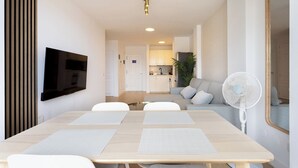 A modern living room with a dining table, white chairs, a flat-screen TV mounted on the wall, a ceiling fan, and a kitchen area in the background. - Home2Book Serenity Terrace & Pool, La Quinta (Tenerife)