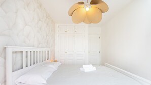 A bedroom with a white bed, a headboard, a wall with a textured pattern, and a ceiling light fixture. - Home2Book Serenity Terrace & Pool, La Quinta (Tenerife)