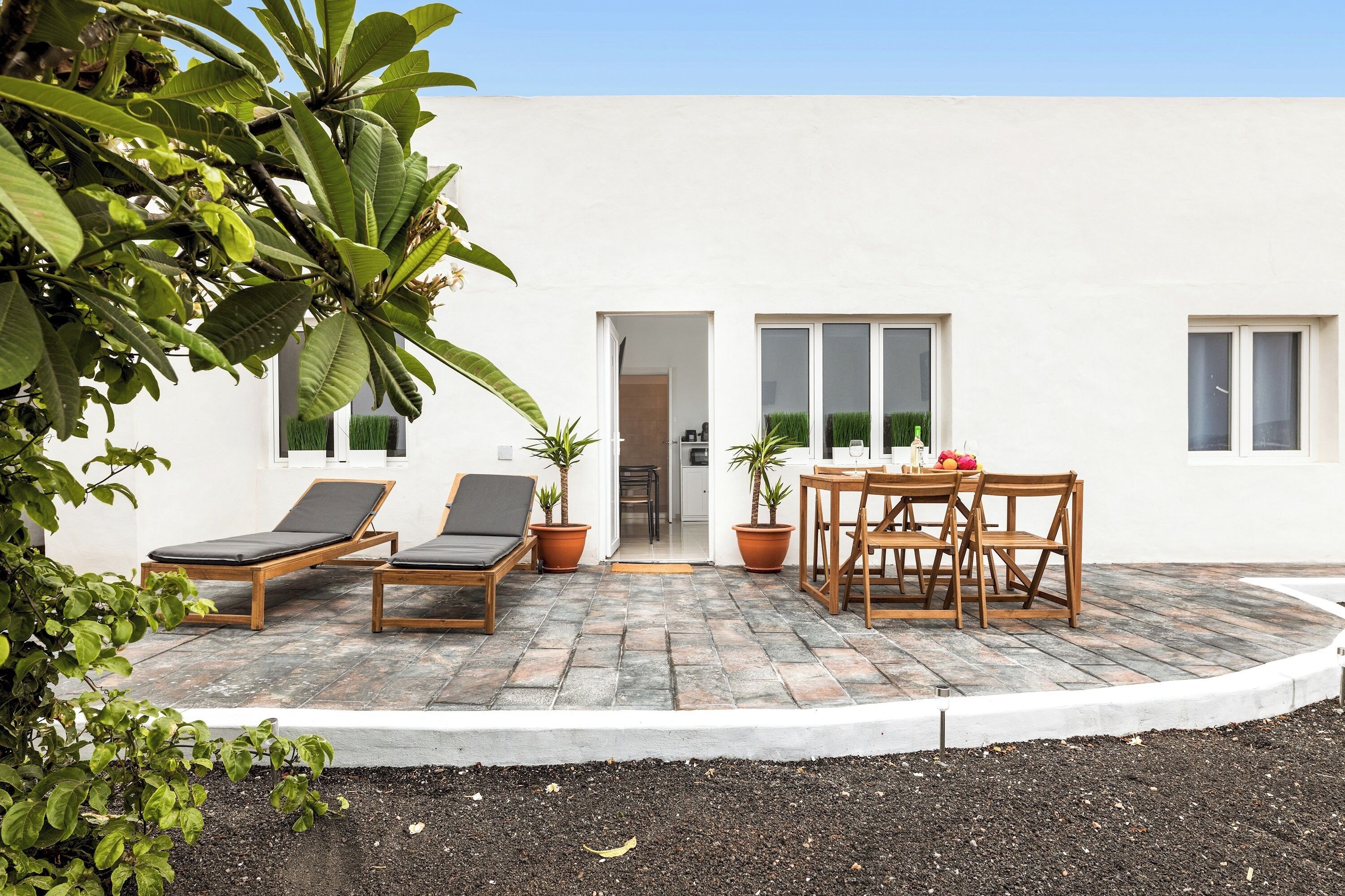Un patio con dos sillones, una mesa con sillas y macetas con plantas.