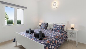 Un dormitorio con una cama, dos mesitas de noche, una lámpara de pared y una ventana con vistas a zonas verdes.