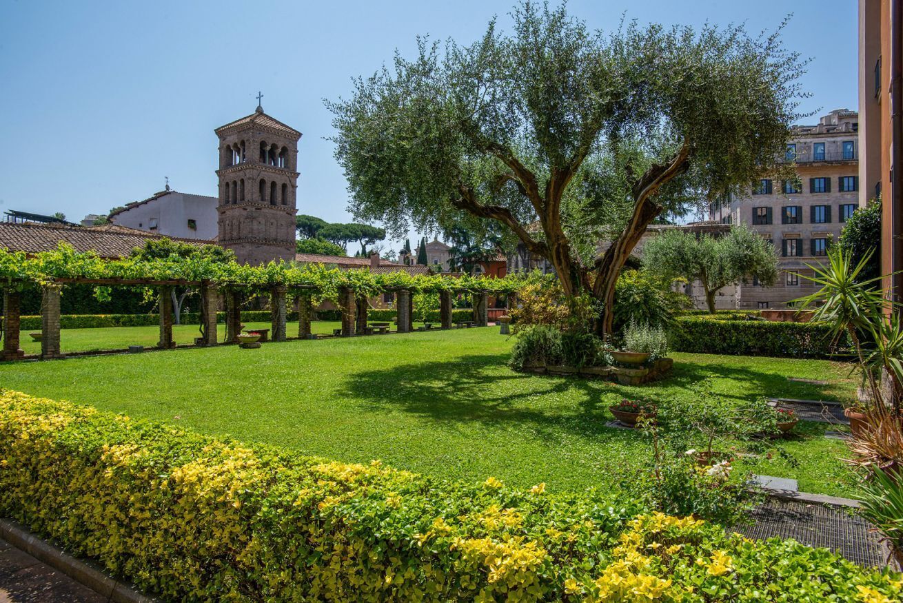 A courtyard with a large tree, a bell tower, and neatly trimmed hedges.