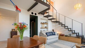 A modern living room with a wooden dining table, beige chairs, a white sofa, a patterned rug, and a staircase with black railings. - TreasureRome Forum Rooftop Terrace Colosseum area • 2BR Duplex (Rome)