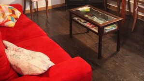 Un salon chaleureux avec un canapé rouge, des chaises en bois, une table basse en verre, un meuble en bois foncé et un téléviseur posé sur le dessus.