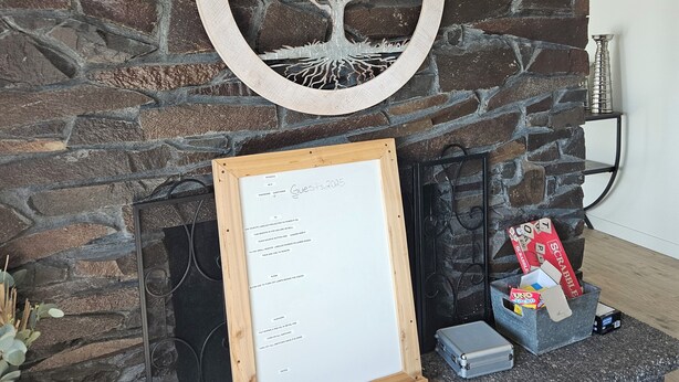 Ein Kamin mit Steinwand, ein gerahmtes Schild mit handgeschriebener Schrift und eine Scrabble-Box auf der Kaminbank.
