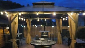Ein Terrassenbereich im Freien mit Tischen und Stühlen, einem runden Tisch in der Mitte und Lichterketten.