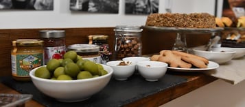 Una mesa con diversos alimentos, incluyendo aceitunas, frascos de conservas y pan.
