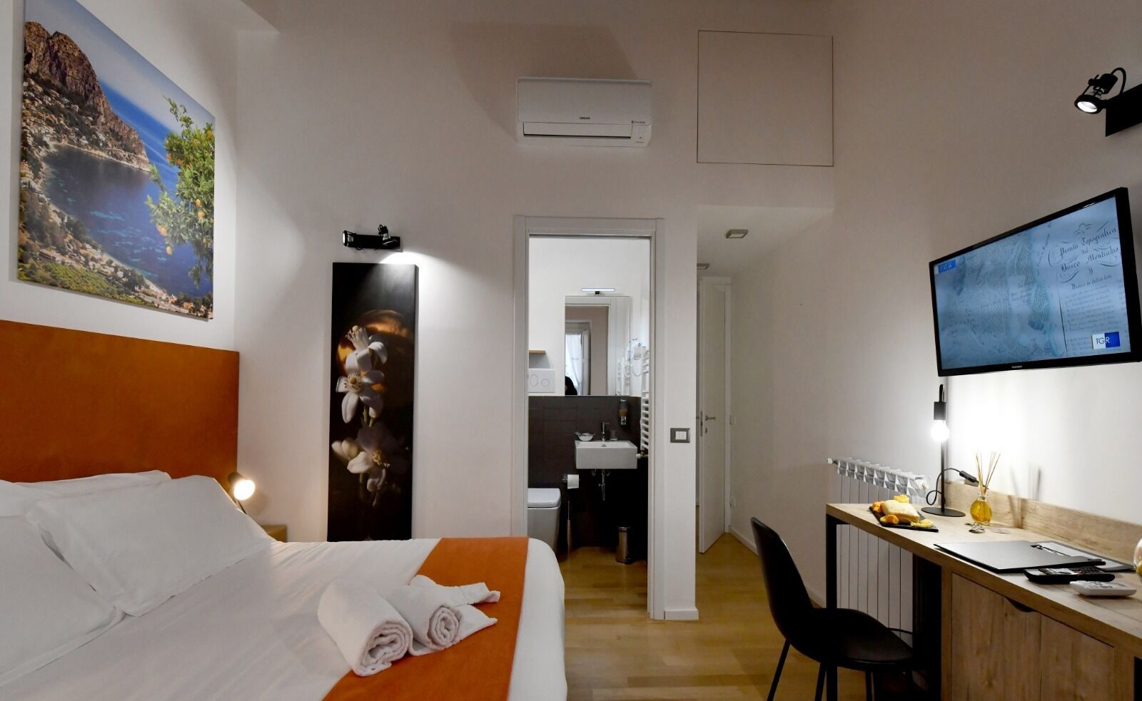 A hotel room with a bed, a desk, a TV, and a bathroom visible through an open door.
