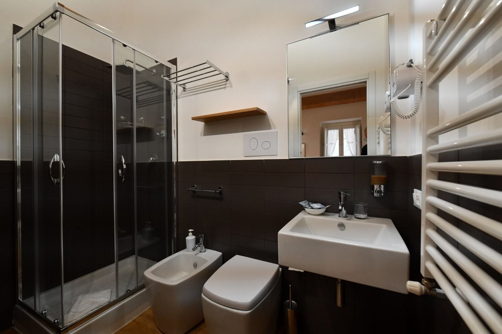 Un baño moderno con cabina de ducha de vidrio, un bidé, un lavabo con espejo y un perchero para toallas.