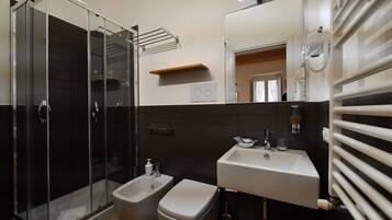 Un baño moderno con cabina de ducha de vidrio, un bidé, un lavabo con espejo y un perchero para toallas.