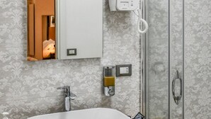 Casa de banho com uma grande pia branca, um espelho, chuveiro e um porta-toalhas.