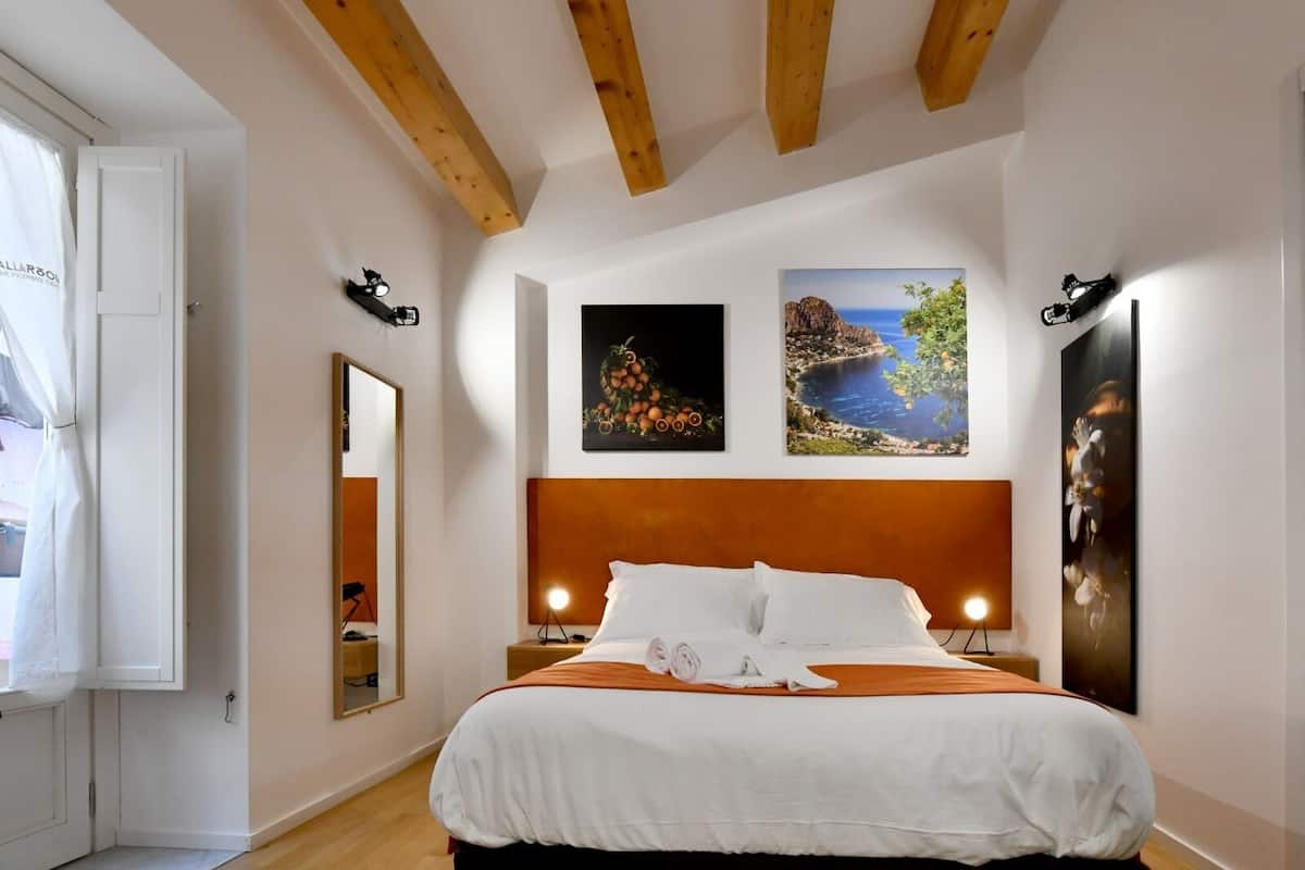 Une chambre d’hôtel avec un plafond en bois, un lit avec une literie blanche et orange, et trois tableaux encadrés accrochés au mur.