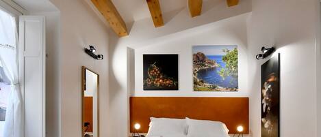 A hotel room with a wooden ceiling, a bed with white and orange bedding, and three framed pictures on the wall.
