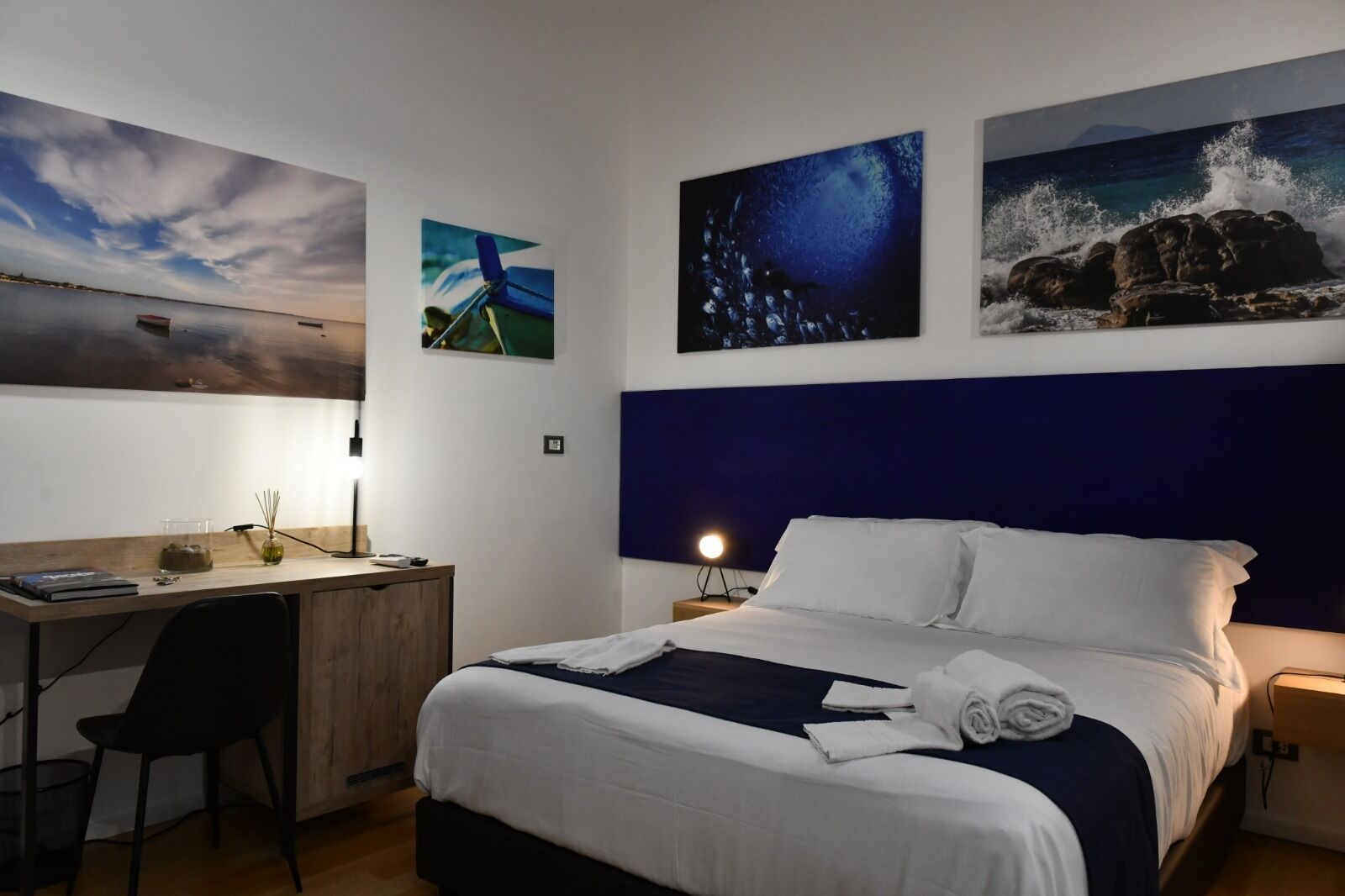 A hotel room with a bed, desk, chair, and artwork on the walls.