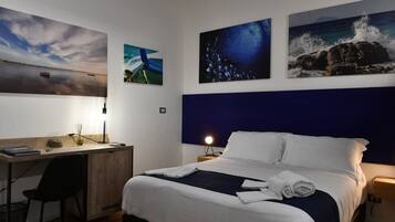 A hotel room with a bed, desk, chair, and artwork on the walls.