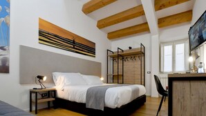 Quarto com cama, escrivaninha, cadeira, televisão e claraboia.