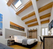 Un dormitorio con cama, escritorio, silla, televisión y tragaluz.