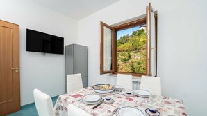 Un comedor con una mesa dispuesta para cuatro personas, un televisor de pantalla plana montado en la pared y una ventana con vistas a zonas verdes.