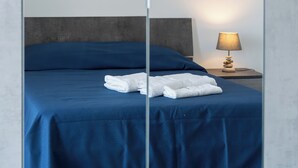 Una cama bien tendida con ropa de cama azul y toallas blancas, una lámpara de noche y una mesita de madera.