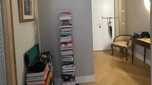 A hallway with a stack of books on a black mat, a framed picture on the wall, a door with a key in the lock, and a chair in the corner.