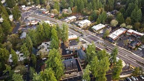 An aerial view of a commercial area with parking lots, roads, and buildings surrounded by dense forest. - Lake Oswego Quiet Ground Level Condo Private Entrance - Pet Friendly! (Lake Oswego)