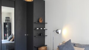 Ett modernt sovrum med en stor säng, en garderob, en spegel, hyllor med dekorativa föremål och en golvlampa.