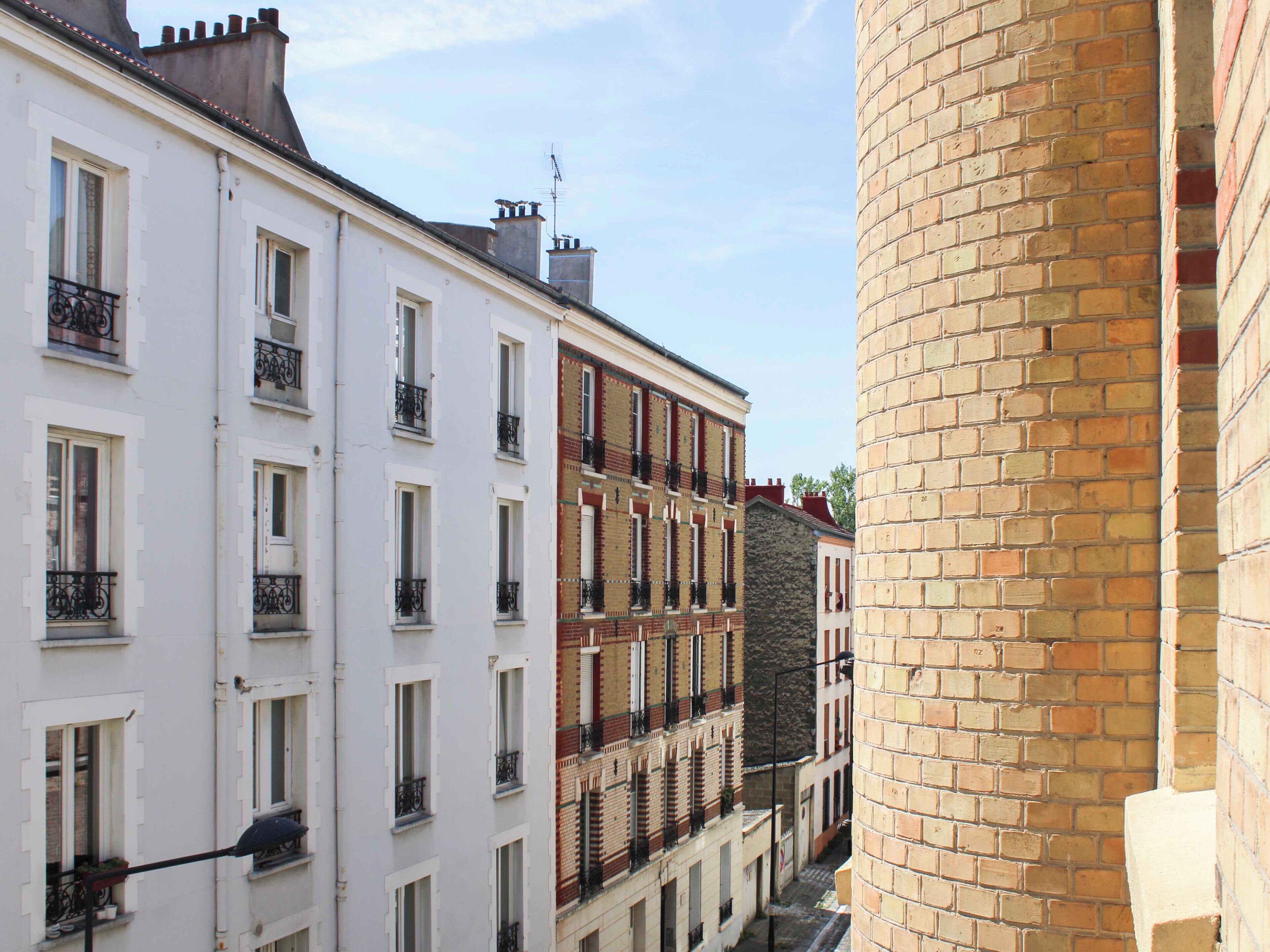 Une rue étroite, bordée de bâtiments de chaque côté, avec des balcons et un mur en briques.