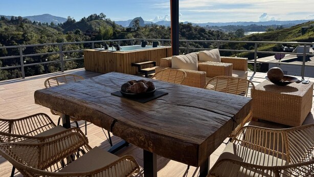 Een houten terras met rieten meubels, een tafel met brood, en uitzicht op bergen.