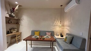 A modern living room with a dining table set for two, a sofa with cushions, a decorative vase, and a hanging light fixture. - Aflora Tulum (Tulum)