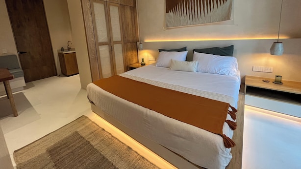 A modern bedroom with a large bed, wooden wardrobe, bedside tables, and a wall-mounted light fixture. - Aflora Tulum (Tulum)
