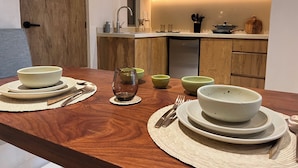 A dining table set with bowls, plates, and cutlery in a modern kitchen with wooden cabinetry and a built-in oven. - Aflora Tulum (Tulum)