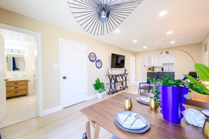 Cocina moderna con armarios blancos, comedor con mesa de madera dispuesta para dos personas, y lámpara de techo.