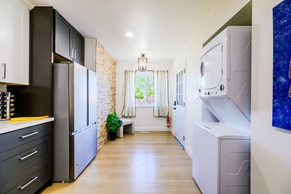 Una cocina estrecha con pared de ladrillo, una ventana con cortinas y una lavadora.