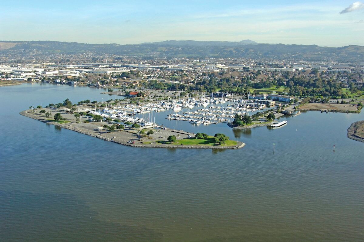 An aerial view of a marina with boats docked, surrounded by a cityscape and hills in the distance.