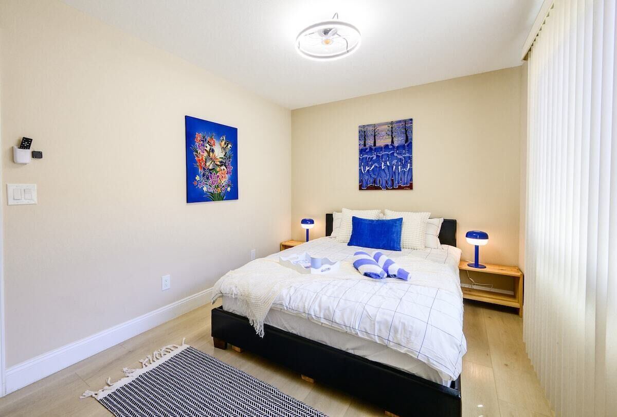 A bedroom with a bed, two bedside tables, a nightstand, a wall-mounted light fixture, and two paintings.