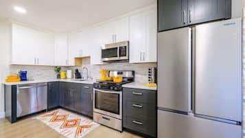 A modern kitchen with stainless steel appliances, white cabinets, and a patterned rug.