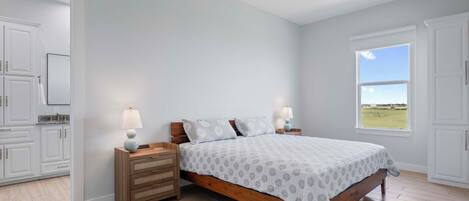 A bedroom with a wooden bed, two bedside tables with lamps, a ceiling fan, and a window with a view of a field.