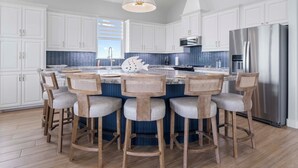 A modern kitchen with white cabinets, a stainless steel refrigerator, and a central island with bar stools. - Unwind on the Bay- Fishing, Pool, Tennis, Basketball courts & Kids' Playground (Palacios)