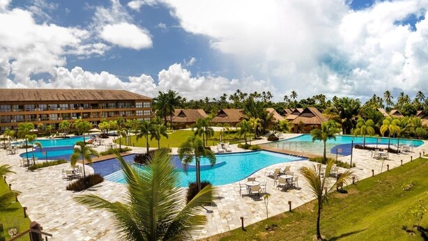 A resort with multiple swimming pools, palm trees, and a large building in the background. - Apt luxo-melhor area de carneiros-Eco Resort-SH092 (Tamandare)