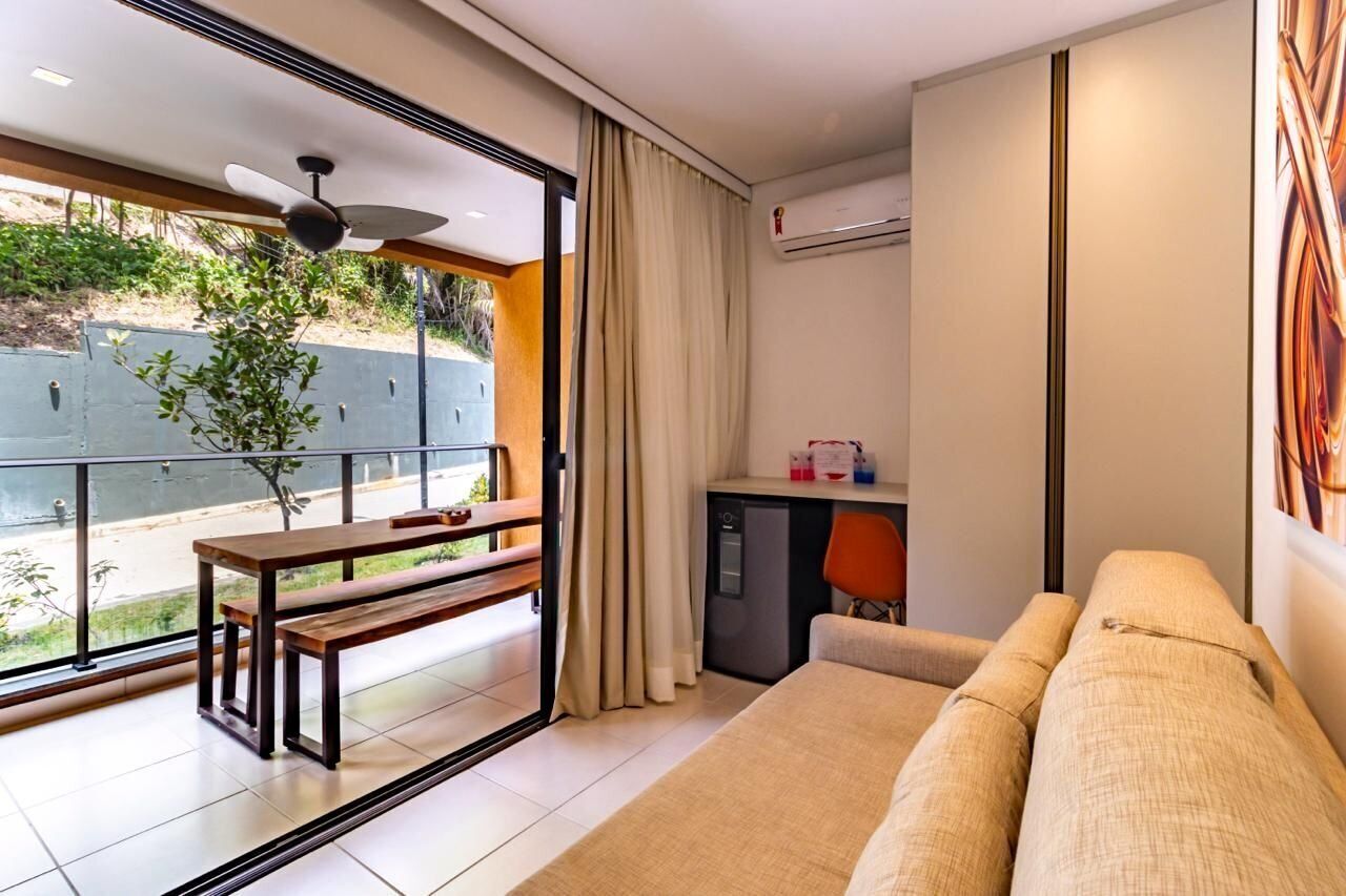 Una habitación de hotel moderna con balcón, sofá, escritorio y una pequeña cocina.