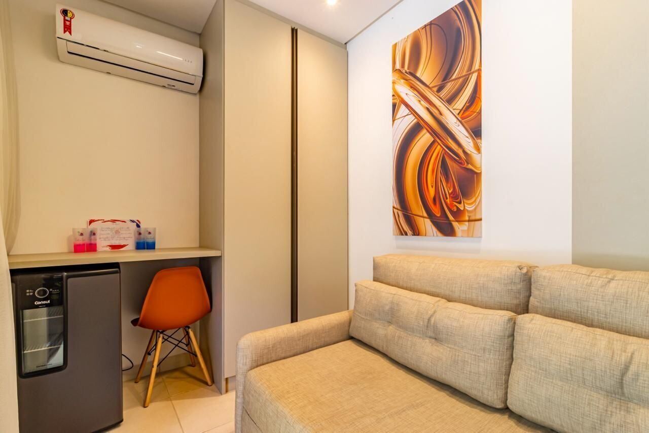 Un espace de vie compact comprenant un coin cuisine, un canapé, un fauteuil orange et un grand tableau abstrait accroché au mur.