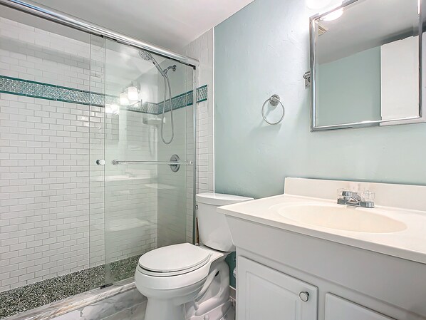 Une salle de bain avec une douche à parois de verre, des toilettes blanches et un lavabo avec un miroir au-dessus.