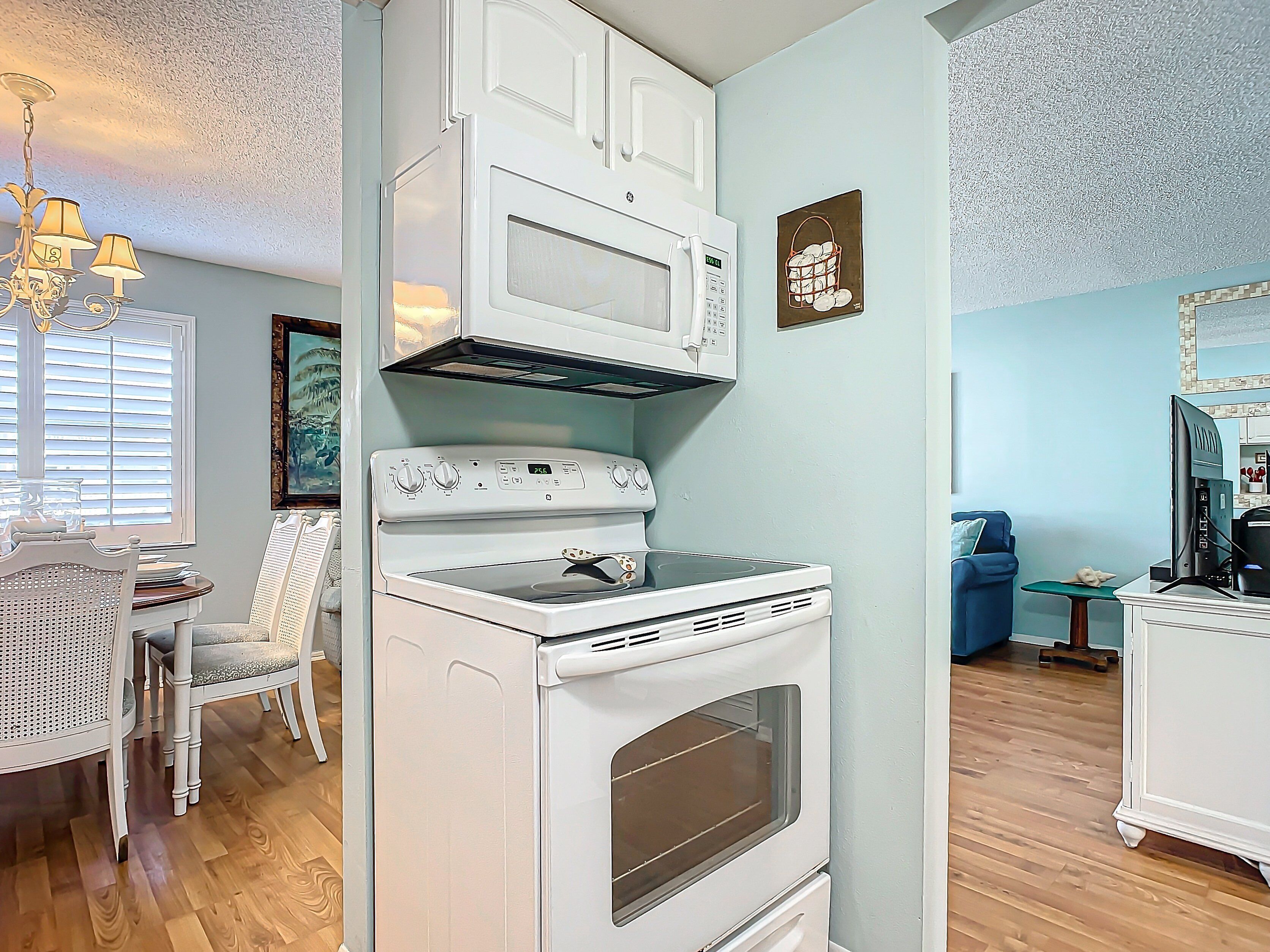 A kitchen with white cabinetry, a stove, and a microwave. There is a dining table with chairs and a chandelier.