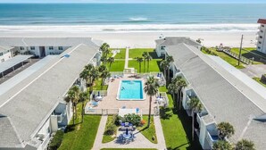 Un hôtel doté d’une piscine entourée de palmiers, offrant une vue sur la plage et disposant d’un parking.