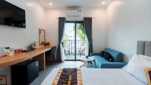 Habitación de hotel con cama, escritorio, televisor, refrigerador pequeño, sofá y balcón con vistas.